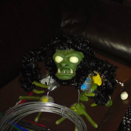 The armature is partially covered in feathery black wool and a green face with protruding teeth has been added 