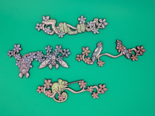 Four wooden charms of creatures on a flowering branch: snake, bats, magpies, chameleon