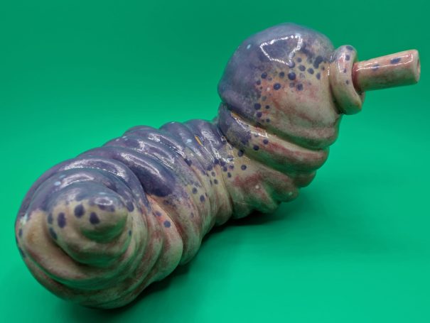 Ceramic sculpture - a fat worm-like creature with proboscosis.  A speckled purple patterning over it's ribbed body