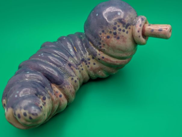 Ceramic sculpture - a fat worm-like creature with proboscosis.  A speckled purple patterning over it's ribbed body
