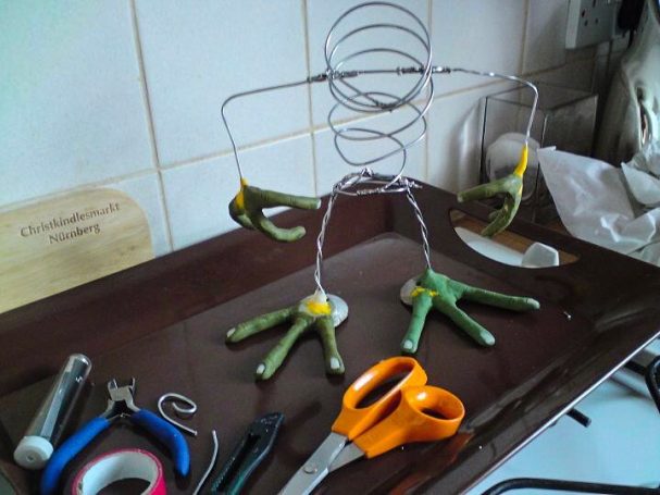 A bare wire armature with green polymer clay extremities 