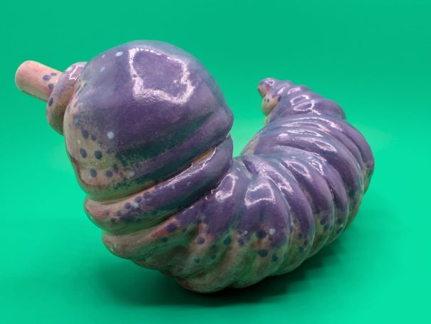 Ceramic sculpture - a fat worm-like creature with proboscosis.  A speckled purple patterning over it's ribbed body