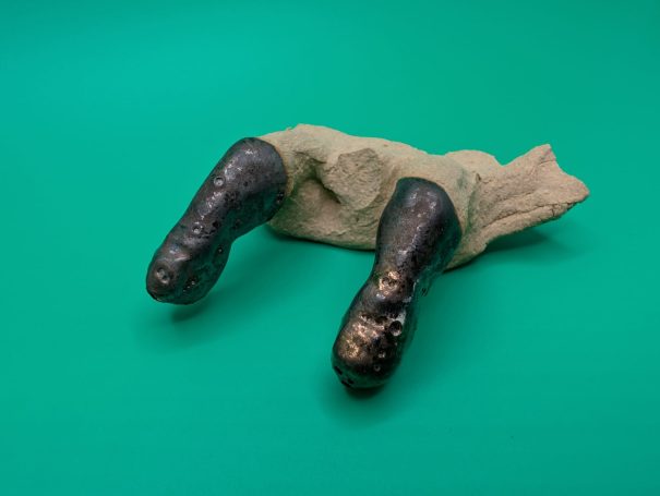 A partial sculpture showing two fingers with a blackened metallic glaze