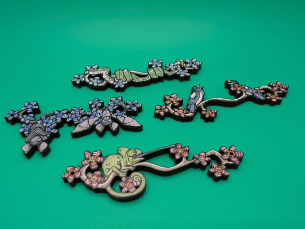 Four wooden charms of creatures on a flowering branch: snake, bats, magpies, chameleon