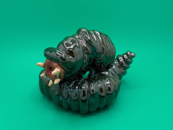 A shiny coiled serpent like sculpture with fleshy mouth and protruding teeth