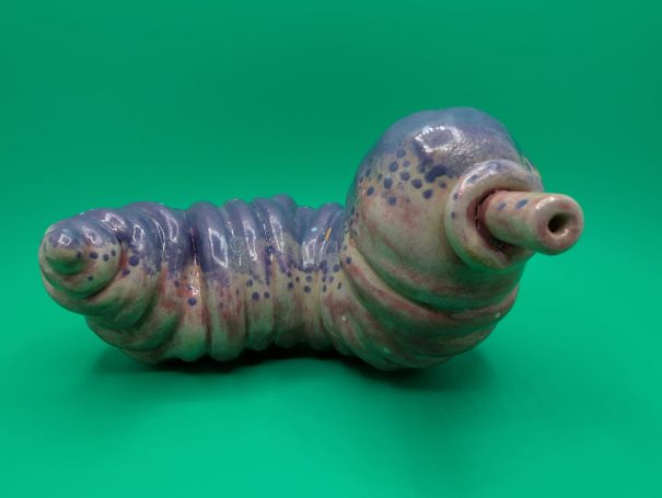 Ceramic sculpture - a fat worm-like creature with proboscosis.  A speckled purple patterning over it's ribbed body
